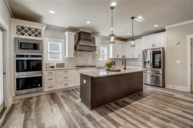 569 White Oak Way, Monroe, GA 30655 - kitchen featuring premium range hood, stainless steel appliances, a kitchen island with sink, a healthy amount of sunlight, and white cabinets