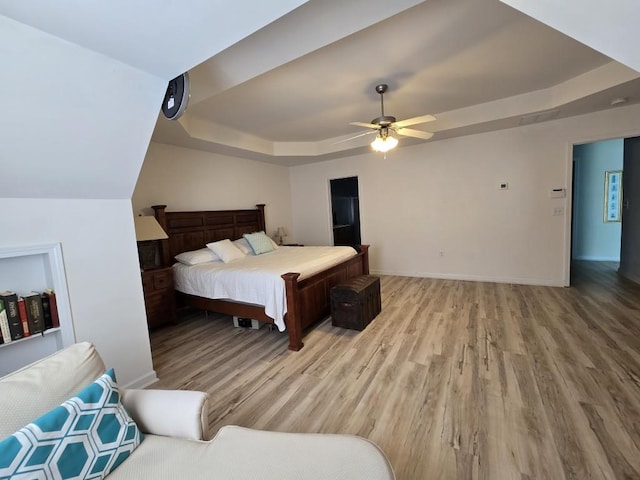 bedroom with ceiling fan, a tray ceiling, and light hardwood / wood-style flooring