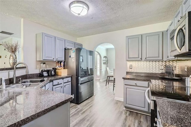 kitchen with appliances with stainless steel finishes, sink, decorative backsplash, light hardwood / wood-style floors, and a textured ceiling