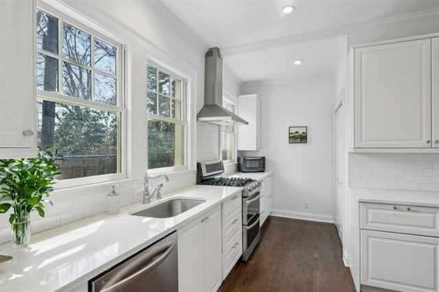 kitchen featuring a sink, white cabinetry, decorative backsplash, wall chimney range hood, and appliances with stainless steel finishes