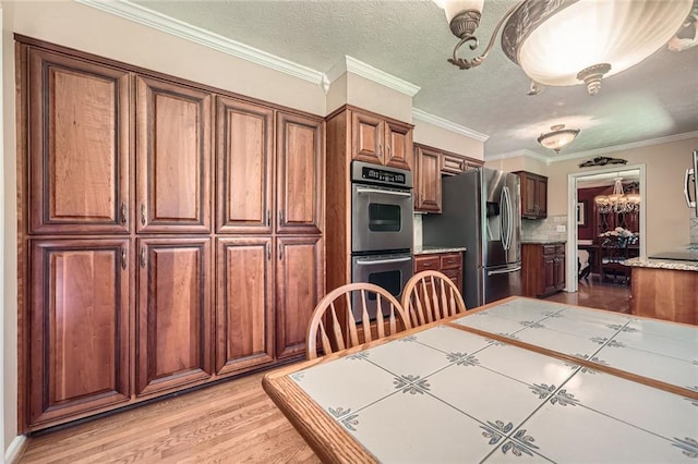 3592 Midvale Cv, Tucker, GA 30084 - kitchen with stainless steel appliances, brown cabinetry, light wood finished floors, ornamental molding, and tile counters