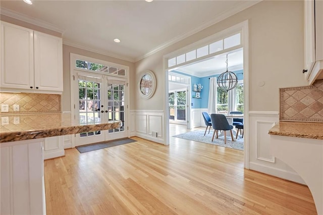 kitchen featuring white cabinets, tasteful backsplash, french doors, decorative light fixtures, and light hardwood / wood-style floors