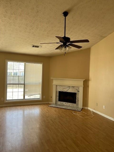 unfurnished living room featuring a fireplace, wood finished floors, visible vents, and a ceiling fan