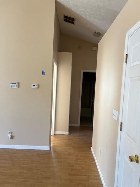 hall with a textured ceiling, light wood-type flooring, visible vents, and baseboards