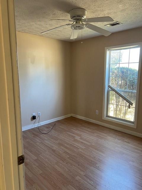 empty room with baseboards, visible vents, ceiling fan, wood finished floors, and a textured ceiling