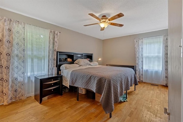 bedroom with a textured ceiling, ceiling fan, and light wood-type flooring