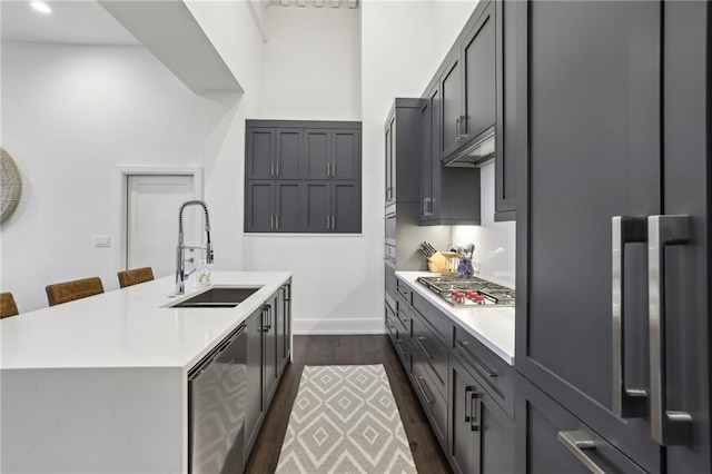 kitchen with dark wood-style flooring, light countertops, appliances with stainless steel finishes, a kitchen island with sink, and a sink