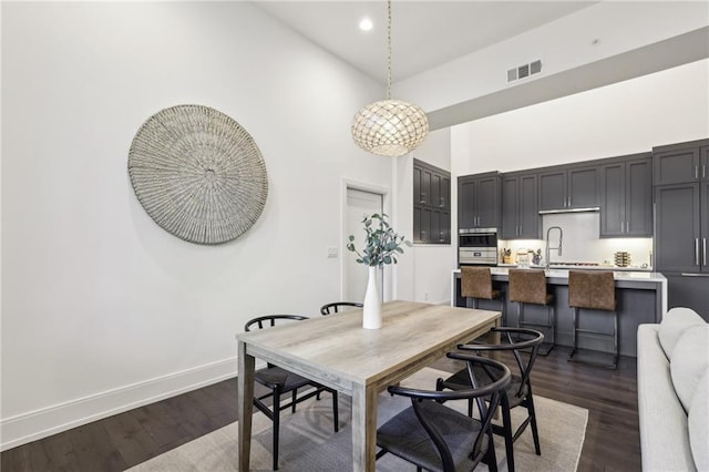 dining room featuring a towering ceiling, dark wood finished floors, visible vents, and baseboards