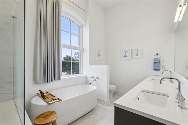 full bathroom with double vanity, toilet, marble finish floor, a freestanding bath, and a sink