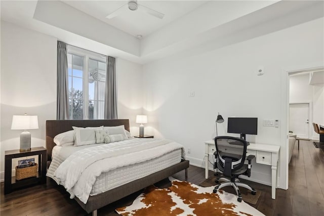 bedroom featuring baseboards, a tray ceiling, and dark wood-style flooring