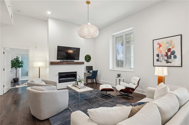 living area featuring a glass covered fireplace, dark wood-style flooring, baseboards, and recessed lighting