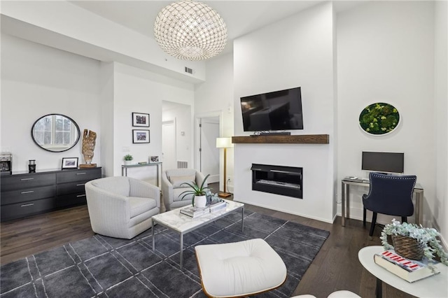 living area featuring a chandelier, dark wood-style flooring, a glass covered fireplace, and a towering ceiling