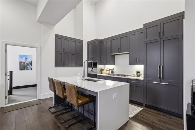 kitchen featuring dark wood-style floors, stainless steel gas cooktop, a sink, and a towering ceiling