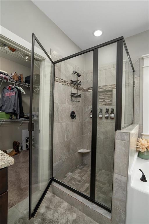 2103 Sourwood Ct, Monroe, GA 30656 - bathroom with a stall shower, a spacious closet, a bath, vanity, and recessed lighting