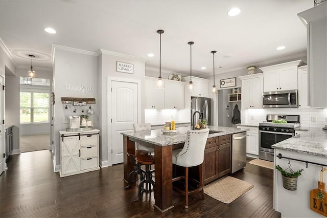 2103 Sourwood Ct, Monroe, GA 30656 - kitchen with stainless steel appliances, crown molding, a kitchen island with sink, tasteful backsplash, and white cabinets
