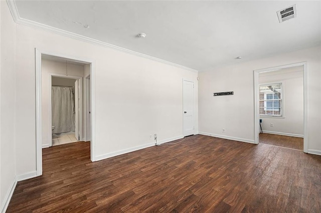 unfurnished room featuring dark wood-style flooring, visible vents, crown molding, and baseboards