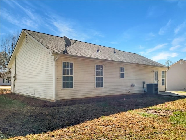 rear view of property with central AC, a yard, and a shingled roof