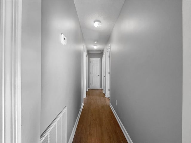 hall with visible vents, a textured ceiling, baseboards, attic access, and dark wood-style flooring