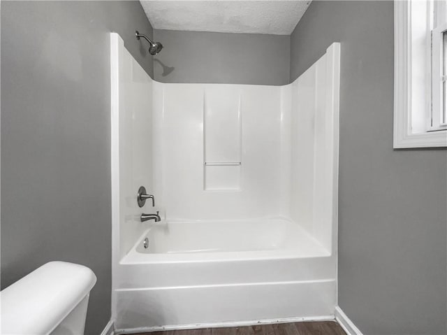 full bath featuring wood finished floors, baseboards, bathtub / shower combination, a textured ceiling, and toilet