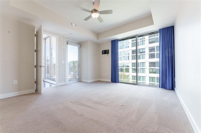 carpeted empty room featuring baseboards, floor to ceiling windows, a tray ceiling, and ceiling fan