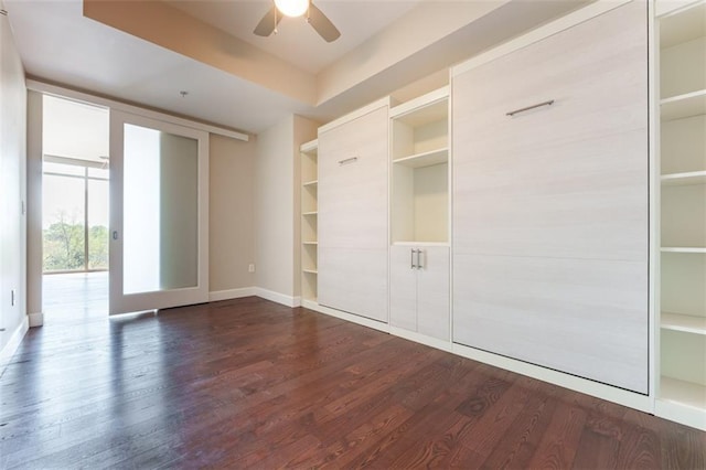 unfurnished bedroom featuring baseboards, expansive windows, a ceiling fan, and dark wood finished floors