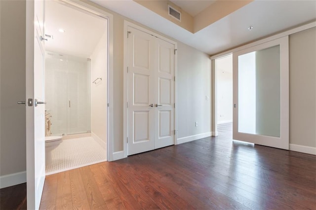 unfurnished bedroom featuring dark wood-type flooring, baseboards, visible vents, and ensuite bath