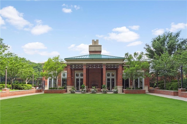 back of property featuring brick siding, a chimney, french doors, and a yard