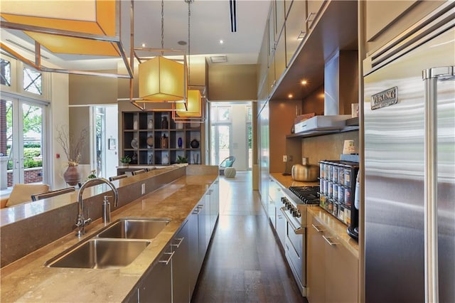 kitchen featuring high end appliances, light stone counters, a sink, wall chimney exhaust hood, and modern cabinets