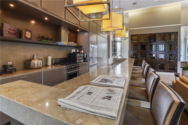 kitchen with high end appliances, a sink, open shelves, wall chimney exhaust hood, and decorative backsplash