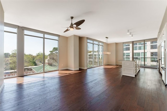 unfurnished living room featuring a wall of windows, ceiling fan, baseboards, and dark wood-style flooring