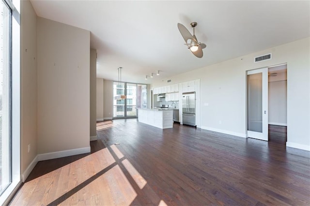 unfurnished living room with a ceiling fan, dark wood-style floors, baseboards, and visible vents
