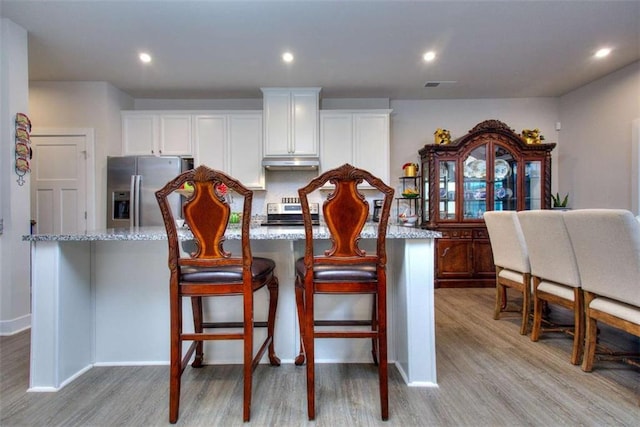 kitchen with light stone counters, stainless steel appliances, an island with sink, and a kitchen bar