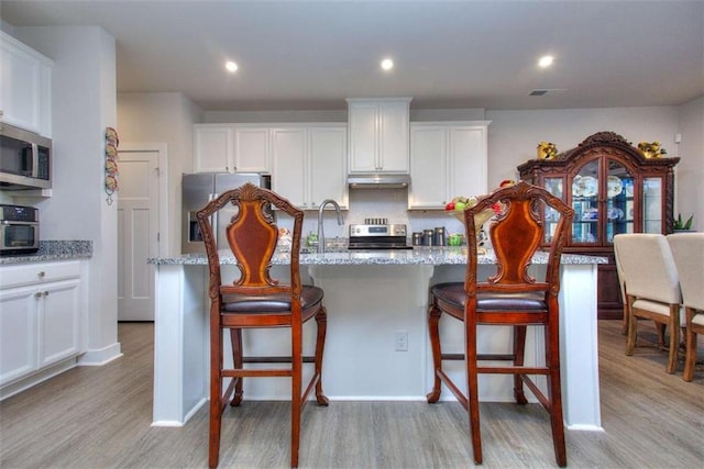 kitchen featuring a kitchen island with sink, a breakfast bar area, light stone countertops, and stainless steel appliances