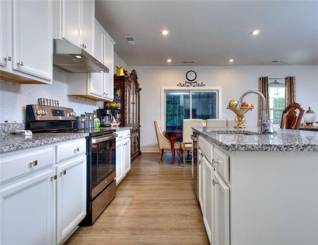 kitchen featuring an island with sink, sink, white cabinets, stainless steel range with electric cooktop, and light stone counters