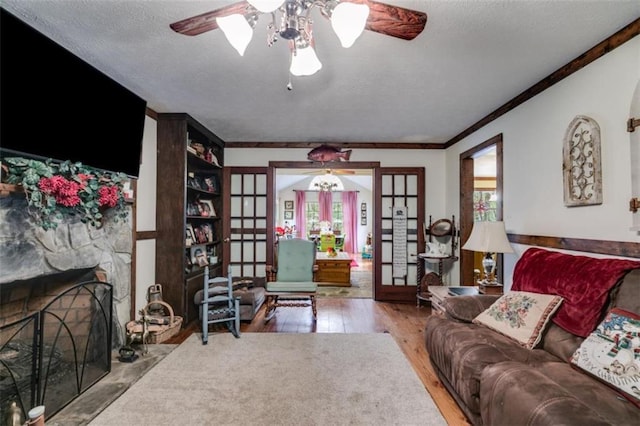 living room with french doors, a stone fireplace, ceiling fan, a textured ceiling, and wood-type flooring