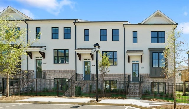 townhome / multi-family property with a fenced front yard, stucco siding, and brick siding