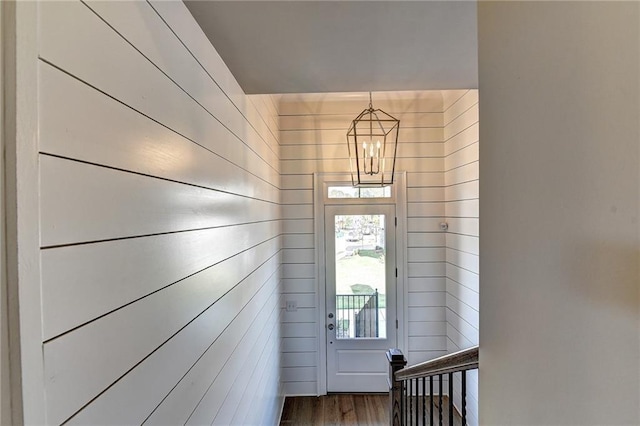 doorway with wood walls, a notable chandelier, and wood finished floors