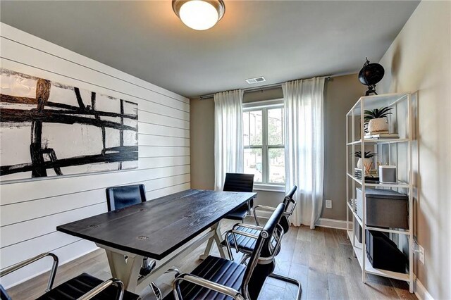 office area with wood walls, visible vents, baseboards, and wood finished floors