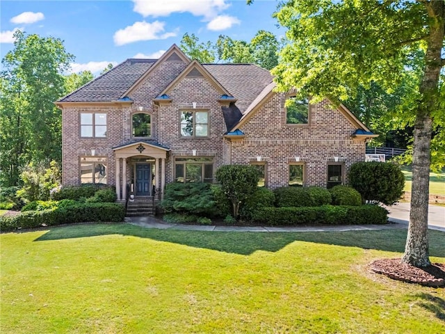 view of front of home featuring brick siding, a front yard, and a shingled roof
