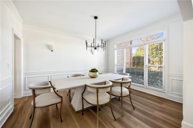 dining room featuring ornamental molding, a decorative wall, a chandelier, wainscoting, and wood finished floors