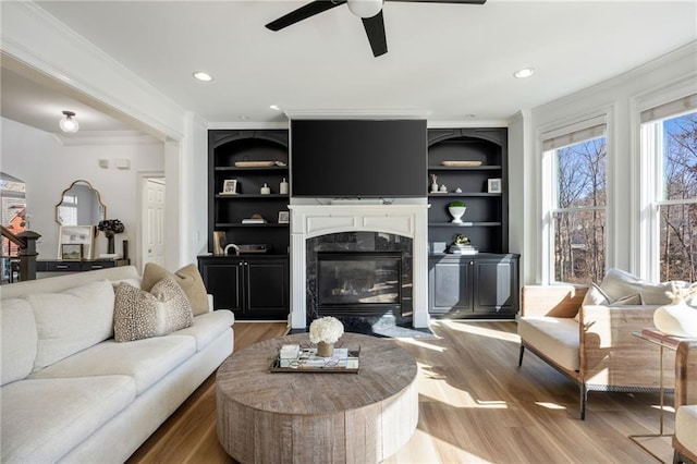 living room with a ceiling fan, a fireplace, ornamental molding, light wood finished floors, and built in shelves