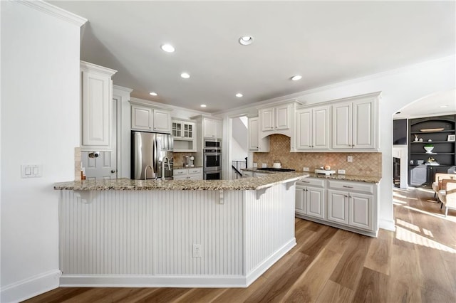 kitchen featuring appliances with stainless steel finishes, arched walkways, a peninsula, a breakfast bar, and light wood-type flooring