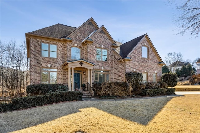 traditional-style house featuring brick siding, a front yard, and a shingled roof