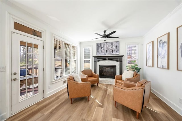 living area with baseboards, a ceiling fan, a glass covered fireplace, light wood-style floors, and ornamental molding