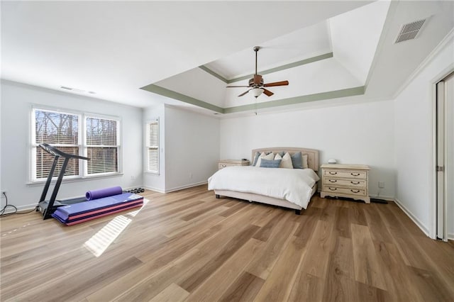 bedroom with a tray ceiling, light wood-type flooring, ceiling fan, baseboards, and crown molding