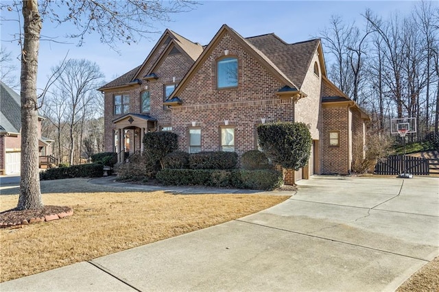 traditional-style home featuring brick siding, driveway, a garage, and roof with shingles