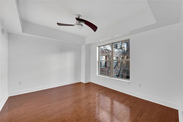 empty room featuring a tray ceiling, ceiling fan, and dark hardwood / wood-style floors