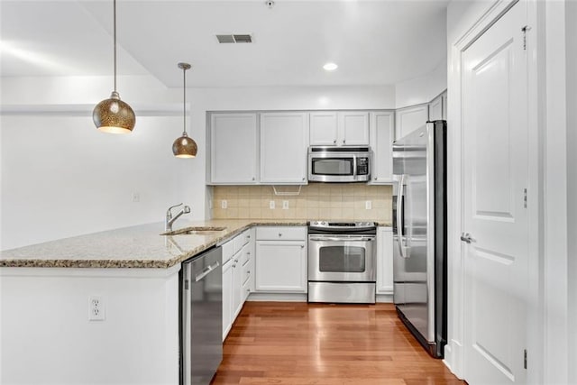 kitchen with sink, appliances with stainless steel finishes, tasteful backsplash, decorative light fixtures, and kitchen peninsula