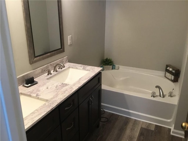 full bathroom featuring a bath, double vanity, wood finished floors, and a sink