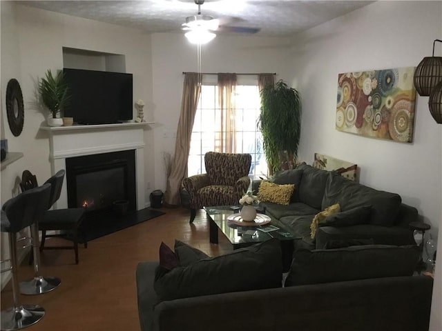 living room featuring a warm lit fireplace, ceiling fan, and wood finished floors